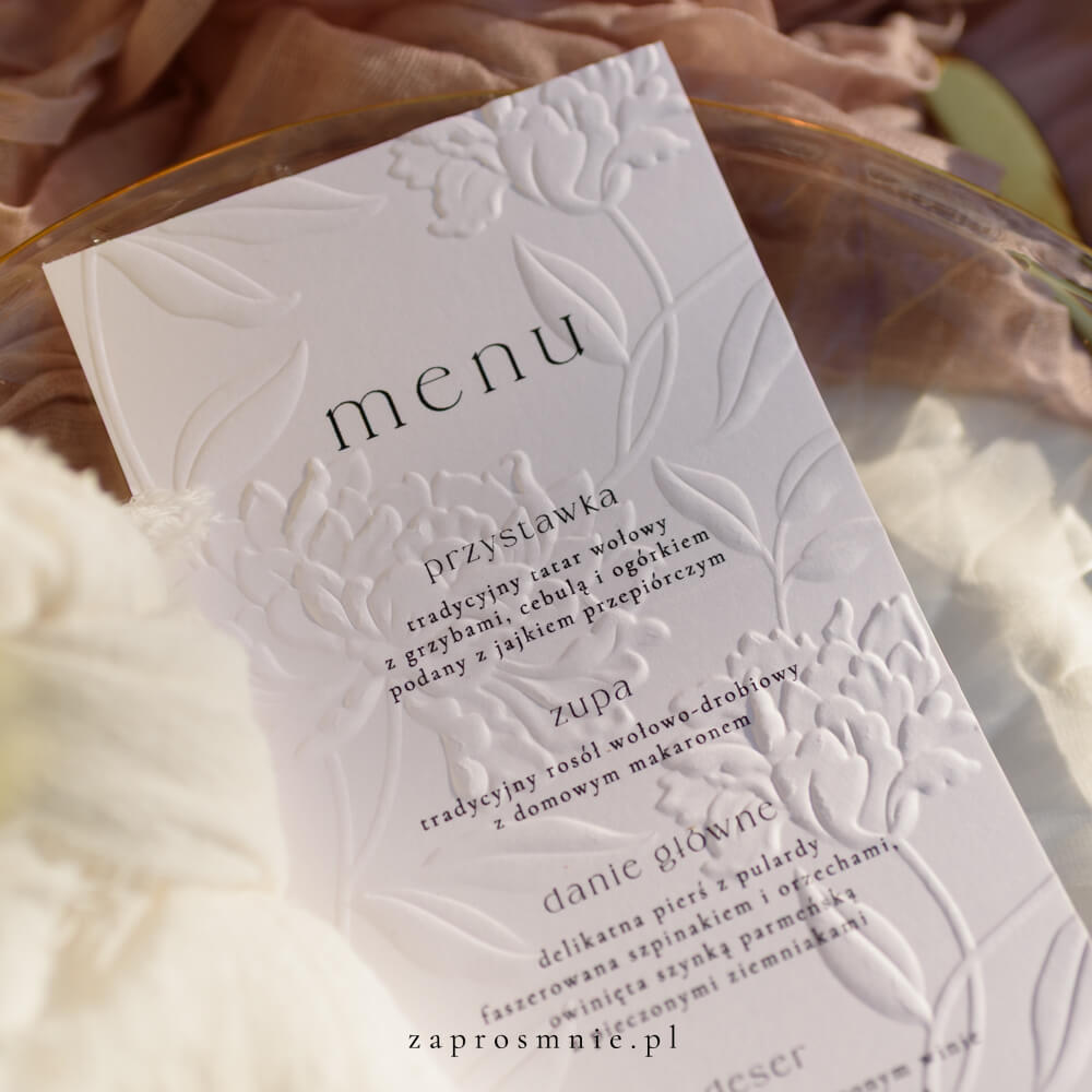 menu weselne z eleganckim tłoczeniem kwiatowym, położone na przezroczystym talerzu ze złotymi sztućcami, subtelna i klasyczna papeteria ślubna z minimalistyczną typografią, dodająca wyjątkowego charakteru aranżacji stołu i spójnej oprawie całego przyjęcia weselnego, menu z tłoczeniem kwiatowym