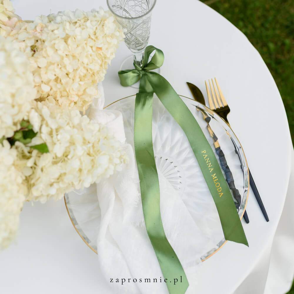Elegancka winietka ślubna w formie zielonej satynowej wstążki z nadrukowanym białym, przewiązana kokardą przy kieliszku, nowoczesna i nietuzinkowa dekoracja stołu weselnego, hit Pinterest i wyjątkowa alternatywa dla klasycznych winietek.